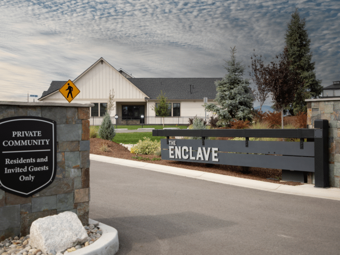 photo showing profile view of The Enclave gate and community wiht a house in the background and clear sunny skies.